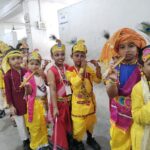 Line of young indian dancers in bright costume headpieces beads and flutes posing in a hallway